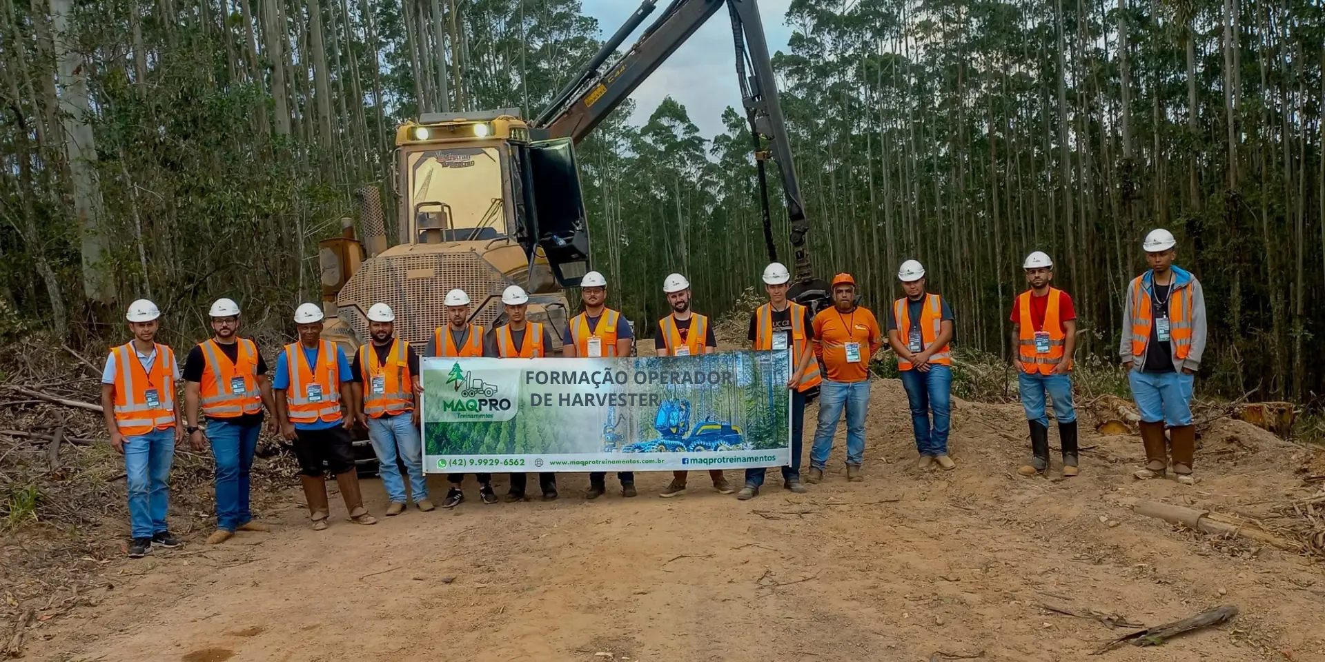 Turma completa da MaqPro em campo, com máquina florestal ao fundo e banner do Curso Operador de Harvester